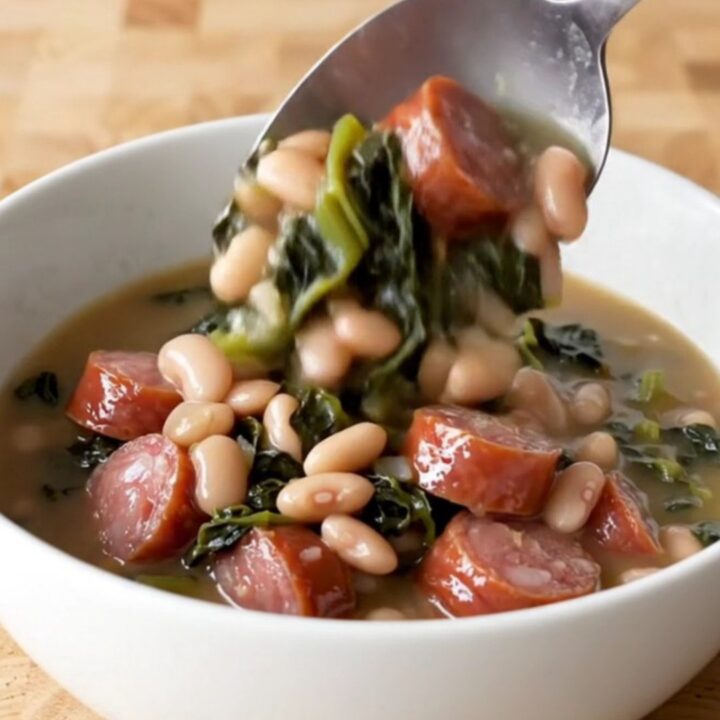A hearty bowl of Southern swamp stew featuring sausage coins, white beans, and dark greens in a rich broth.