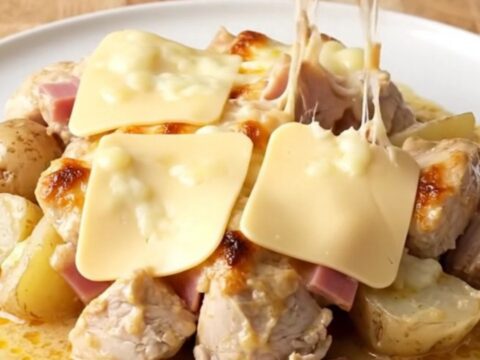 A slow cooker filled with cooked chicken bites, ham, and potatoes covered in a creamy Swiss cheese sauce.