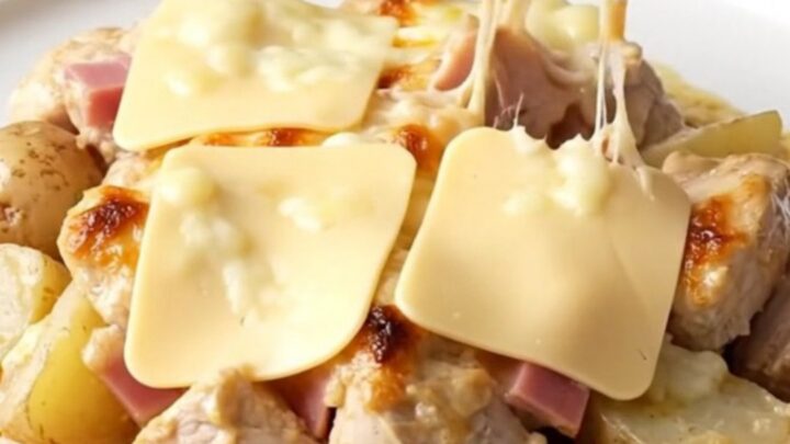 A slow cooker filled with cooked chicken bites, ham, and potatoes covered in a creamy Swiss cheese sauce.
