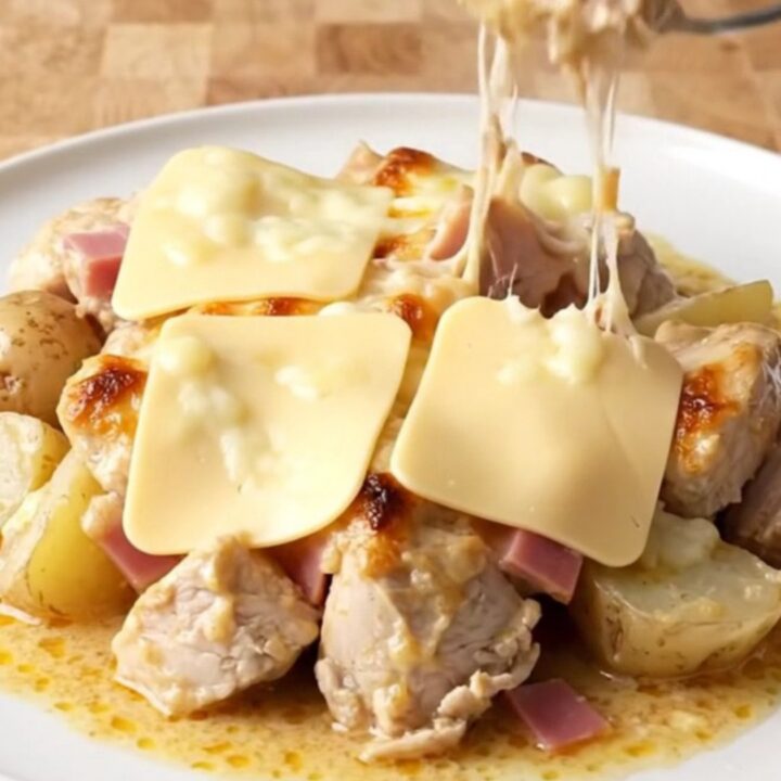 A slow cooker filled with cooked chicken bites, ham, and potatoes covered in a creamy Swiss cheese sauce.