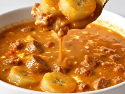 A shallow white bowl filled with creamy orange-red soup containing sausage crumbles and sliced banana peppers.