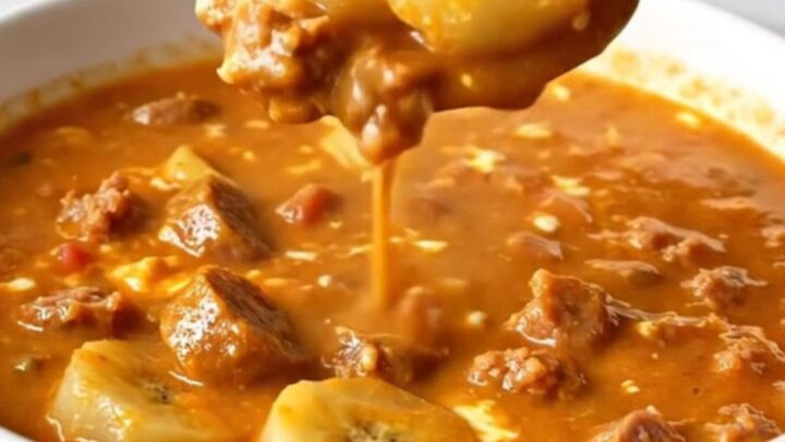 A shallow white bowl filled with creamy orange-red soup containing sausage crumbles and sliced banana peppers.