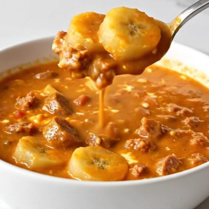 A shallow white bowl filled with creamy orange-red soup containing sausage crumbles and sliced banana peppers.