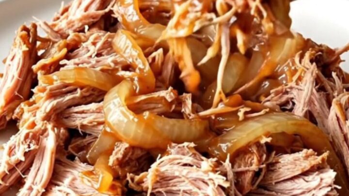 A close-up of tender, shredded pulled pork in a rich barbecue sauce, served on a white plate.