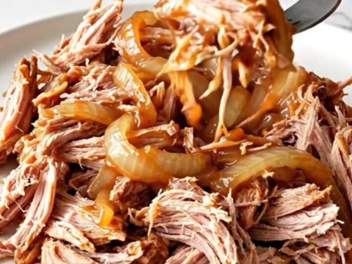 A close-up of tender, shredded pulled pork in a rich barbecue sauce, served on a white plate.