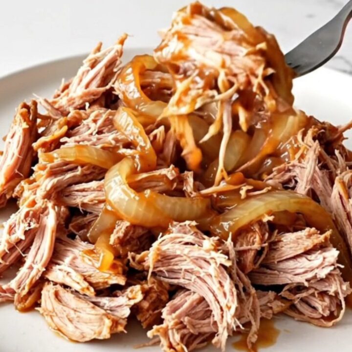 A close-up of tender, shredded pulled pork in a rich barbecue sauce, served on a white plate.