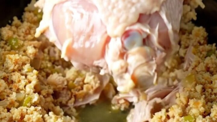 A slow cooker filled with a cooked, golden-tan turkey breast surrounded by moist, herb-flecked cornbread dressing.