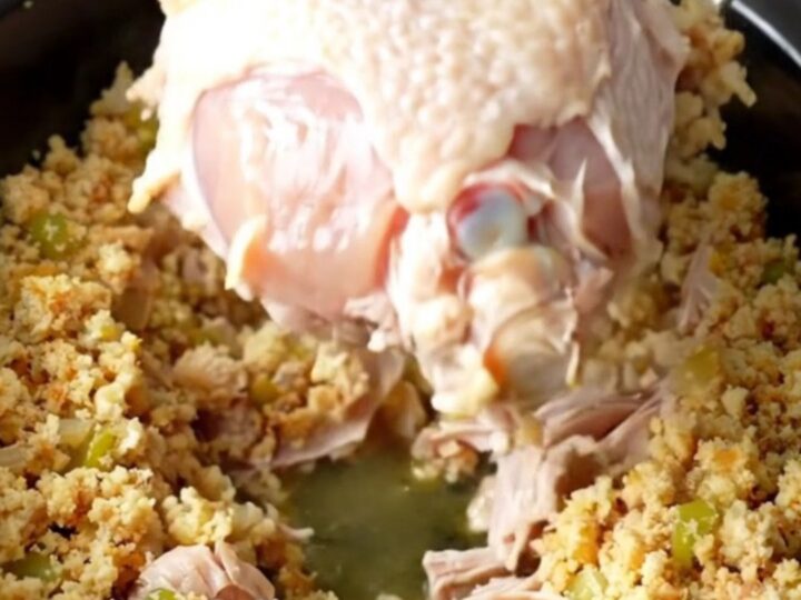 A slow cooker filled with a cooked, golden-tan turkey breast surrounded by moist, herb-flecked cornbread dressing.