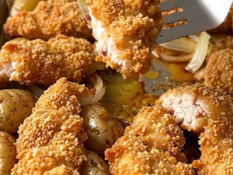 A sheet pan filled with golden pretzel-crusted chicken tenders, roasted baby potatoes, and soft onion wedges.