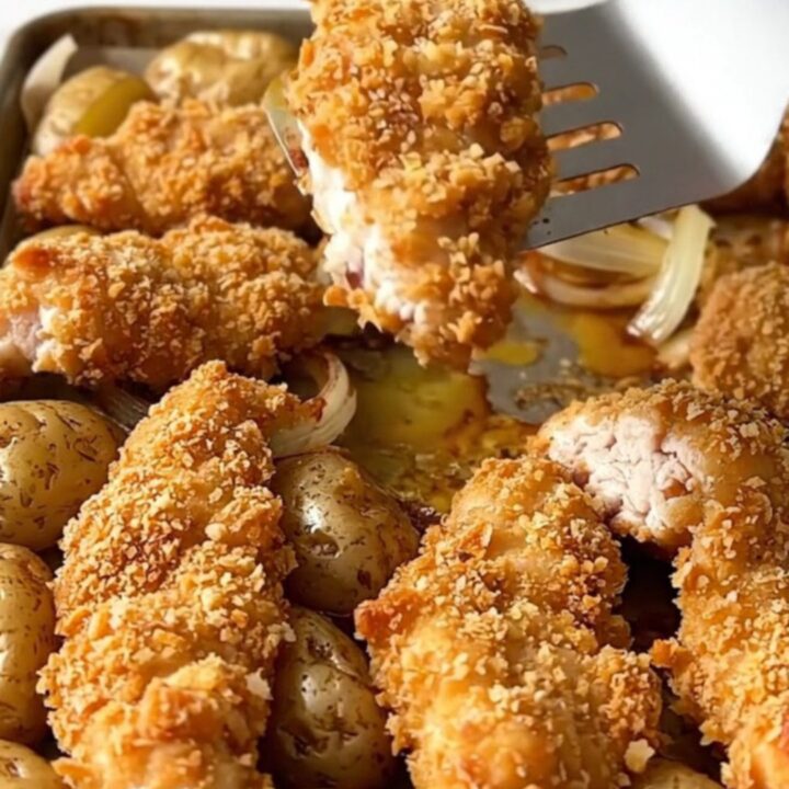 A sheet pan filled with golden pretzel-crusted chicken tenders, roasted baby potatoes, and soft onion wedges.
