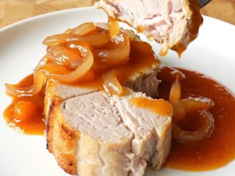 Four thick, cooked pork loin chops covered in a rich, red-orange Catalina sauce and sliced onions.