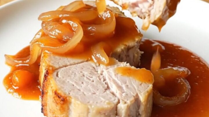 Four thick, cooked pork loin chops covered in a rich, red-orange Catalina sauce and sliced onions.