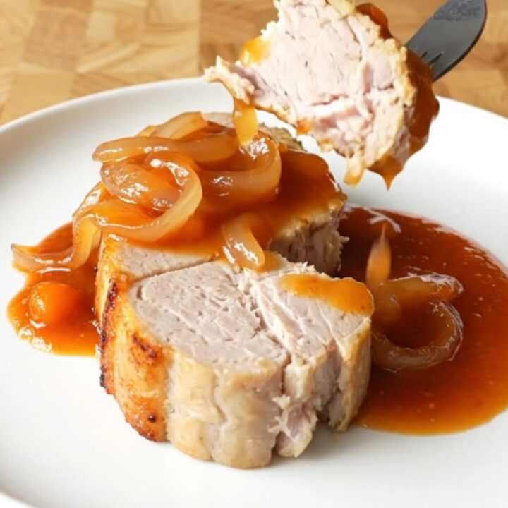 Four thick, cooked pork loin chops covered in a rich, red-orange Catalina sauce and sliced onions.