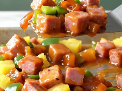 A sheet pan filled with golden-brown ham cubes, bright yellow pineapple, and green pepper chunks with a glossy glaze.