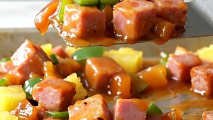 A sheet pan filled with golden-brown ham cubes, bright yellow pineapple, and green pepper chunks with a glossy glaze.