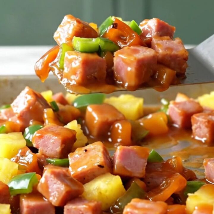 A sheet pan filled with golden-brown ham cubes, bright yellow pineapple, and green pepper chunks with a glossy glaze.
