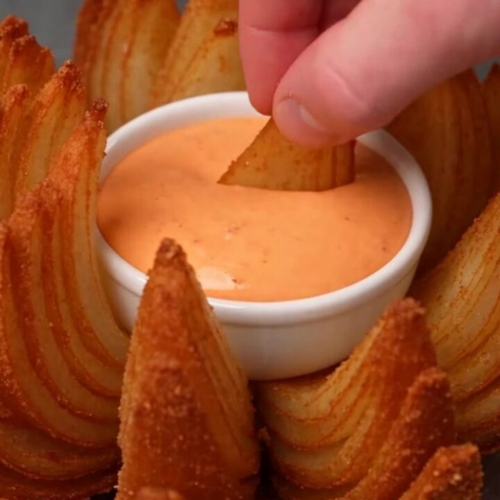 A golden-brown crispy blooming onion served on a white platter with a bowl of remoulade in the center.