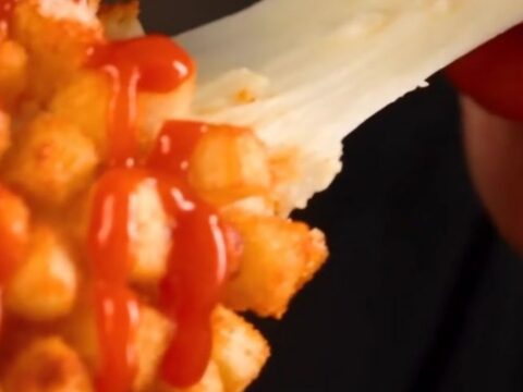 A close-up of a golden-brown crispy potato Korean corn dog being pulled apart to reveal a long