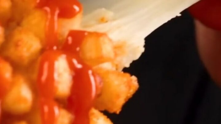 A close-up of a golden-brown crispy potato Korean corn dog being pulled apart to reveal a long