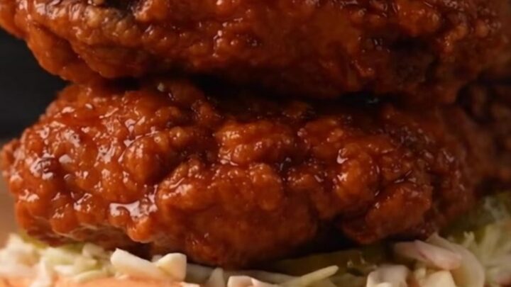 A close-up of a golden-brown Nashville hot honey chicken sandwich with glaze dripping down the side.