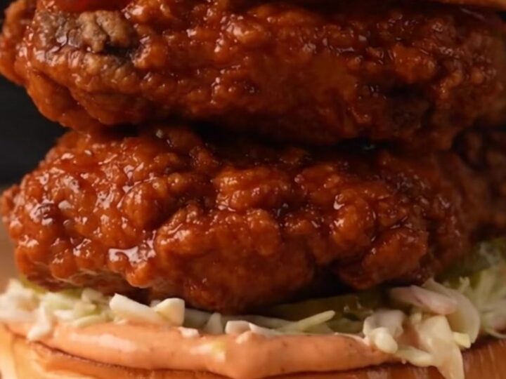A close-up of a golden-brown Nashville hot honey chicken sandwich with glaze dripping down the side.