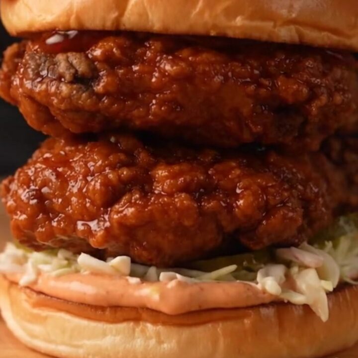 A close-up of a golden-brown Nashville hot honey chicken sandwich with glaze dripping down the side.