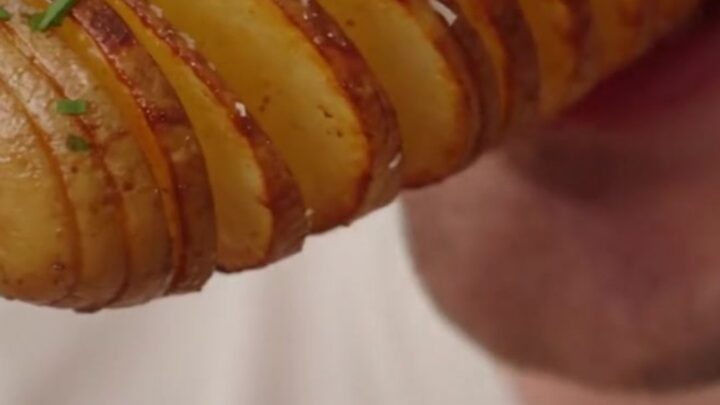 Close up of crispy golden-brown accordion potato skewers garnished with fresh chives on a wooden board.