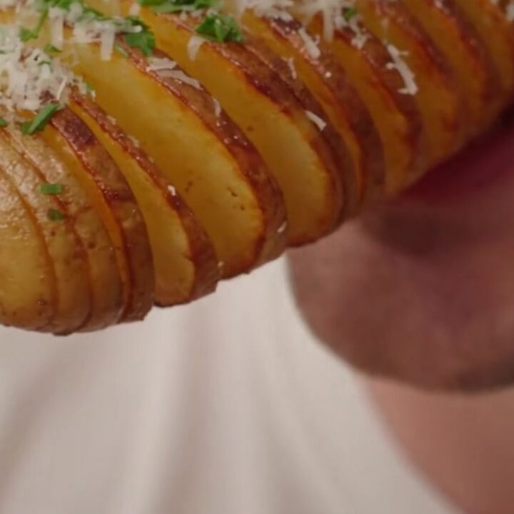 Close up of crispy golden-brown accordion potato skewers garnished with fresh chives on a wooden board.