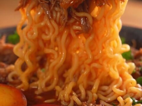 A steaming bowl of birria ramen featuring tender shredded beef, a jammy egg, and fresh cilantro.