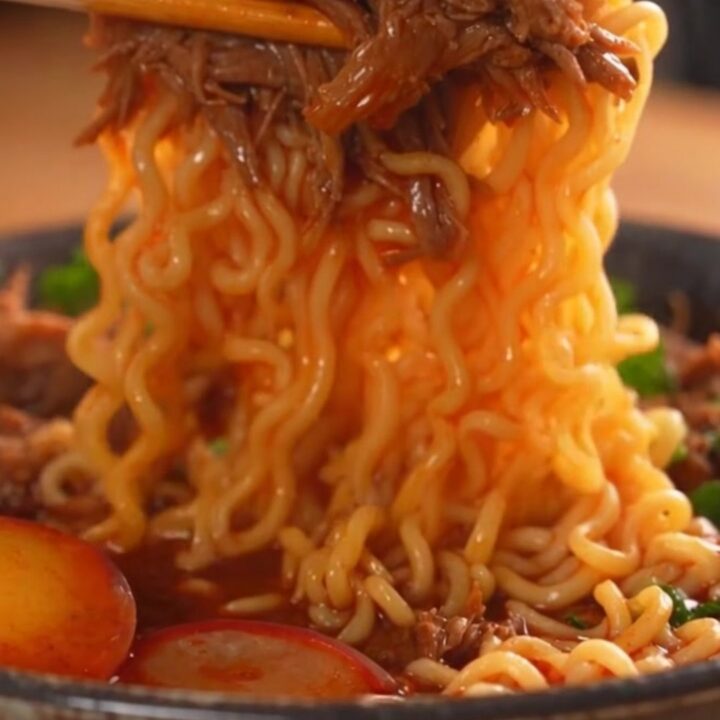 A steaming bowl of birria ramen featuring tender shredded beef, a jammy egg, and fresh cilantro.