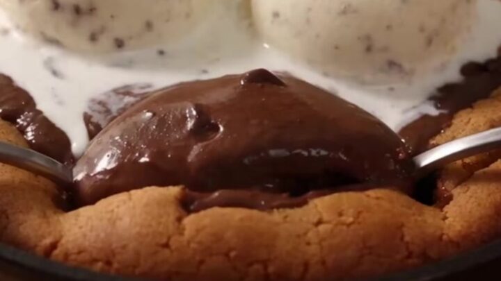 A giant, warm chocolate chip pizookie in an 8-inch cast-iron skillet with melting vanilla ice cream on top.