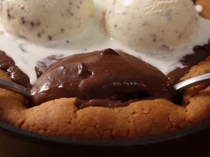 A giant, warm chocolate chip pizookie in an 8-inch cast-iron skillet with melting vanilla ice cream on top.