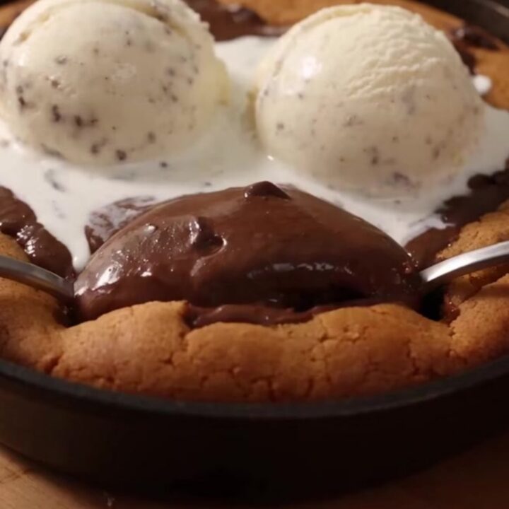A giant, warm chocolate chip pizookie in an 8-inch cast-iron skillet with melting vanilla ice cream on top.
