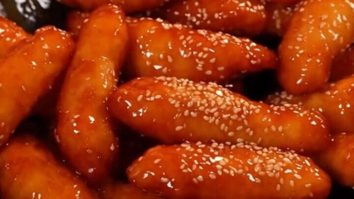 A plate of crispy Korean honey butter chicken tenders glistening with a golden glaze and topped with sesame seeds.