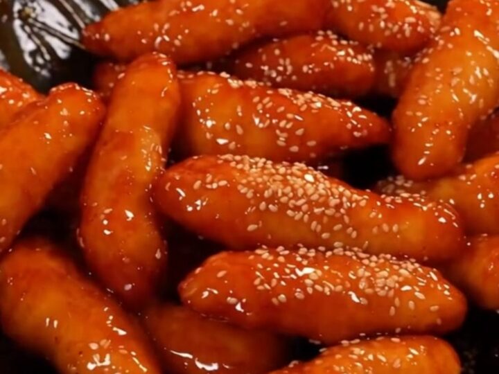 A plate of crispy Korean honey butter chicken tenders glistening with a golden glaze and topped with sesame seeds.