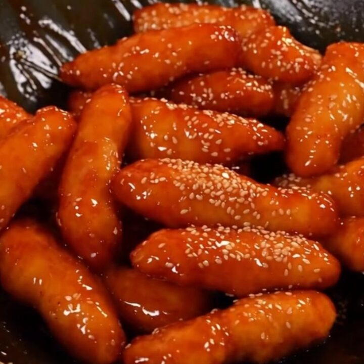 A plate of crispy Korean honey butter chicken tenders glistening with a golden glaze and topped with sesame seeds.