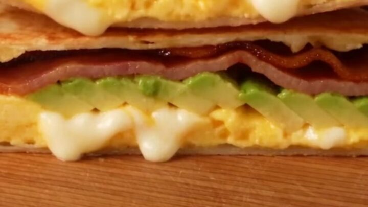 A crispy, golden-brown folded breakfast quesadilla triangle on a marble surface.