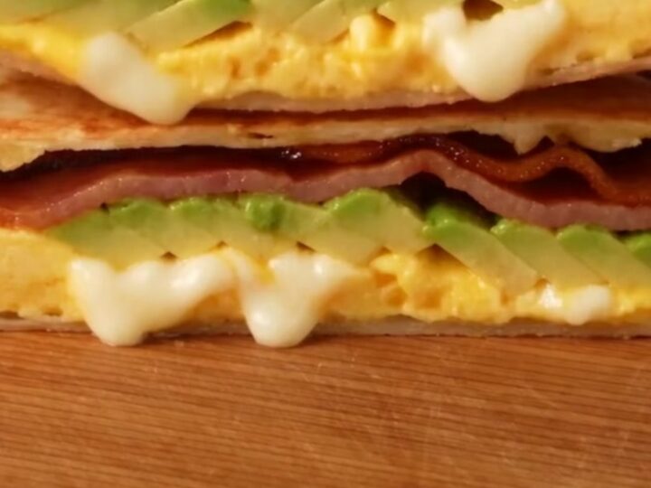A crispy, golden-brown folded breakfast quesadilla triangle on a marble surface.