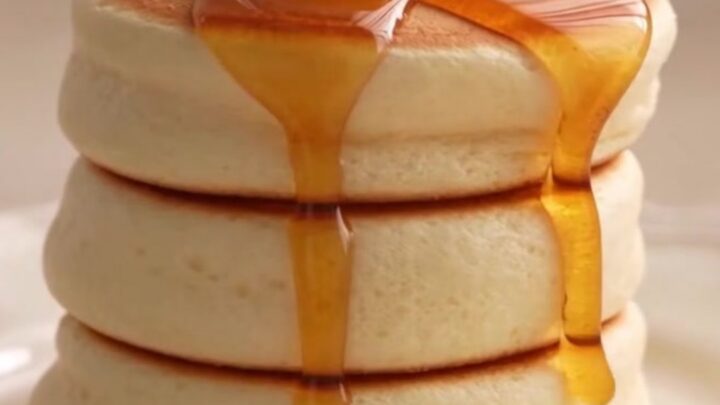 A stack of two fluffy Japanese soufflé pancakes topped with a melting pat of butter and syrup.