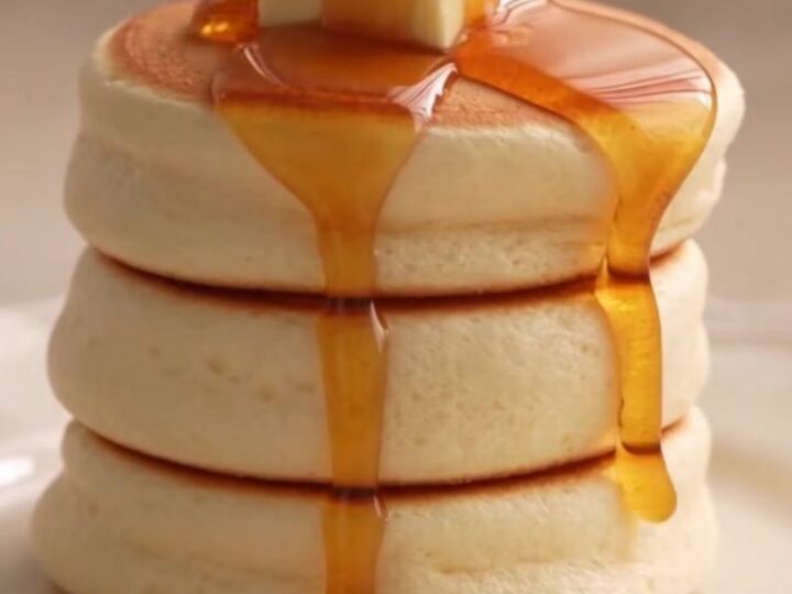 A stack of two fluffy Japanese soufflé pancakes topped with a melting pat of butter and syrup.