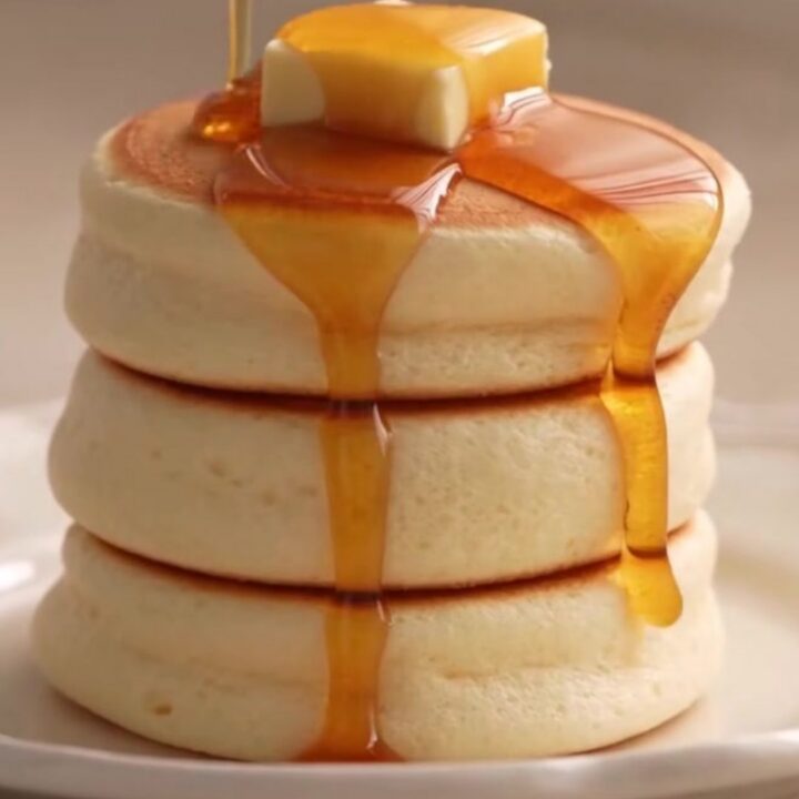 A stack of two fluffy Japanese soufflé pancakes topped with a melting pat of butter and syrup.