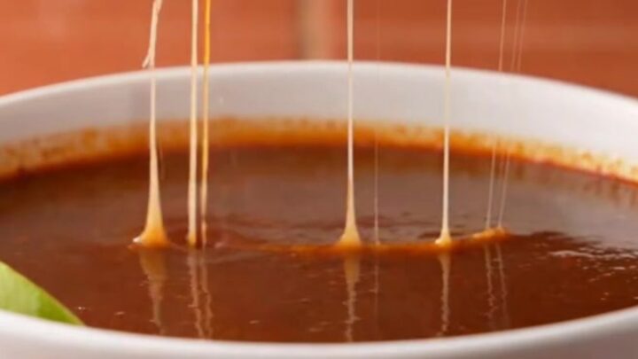 A plate of crispy, golden-brown beef birria quesatacos served with a bowl of rich red consomé.