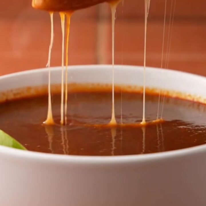 A plate of crispy, golden-brown beef birria quesatacos served with a bowl of rich red consomé.