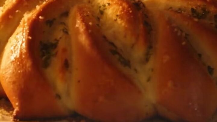 A golden-brown pull-apart garlic herb brioche flower on a wooden board.