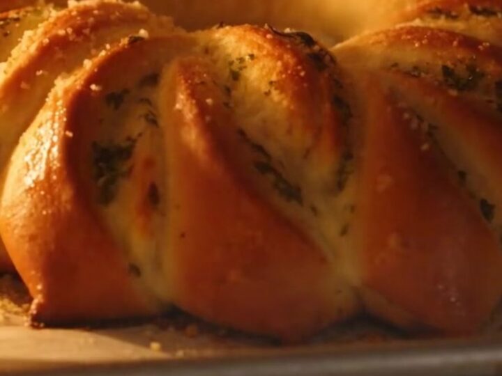 A golden-brown pull-apart garlic herb brioche flower on a wooden board.