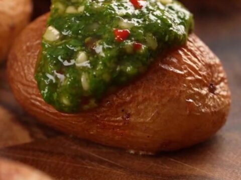 A top-down view of crispy smashed fingerling potatoes on a baking sheet, topped with vibrant green chimichurri sauce.