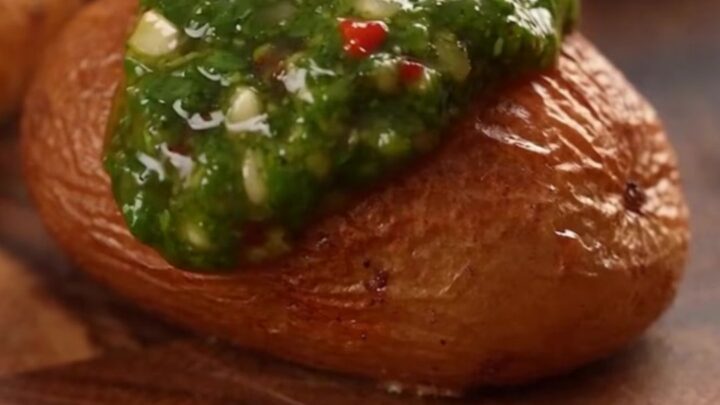A top-down view of crispy smashed fingerling potatoes on a baking sheet, topped with vibrant green chimichurri sauce.