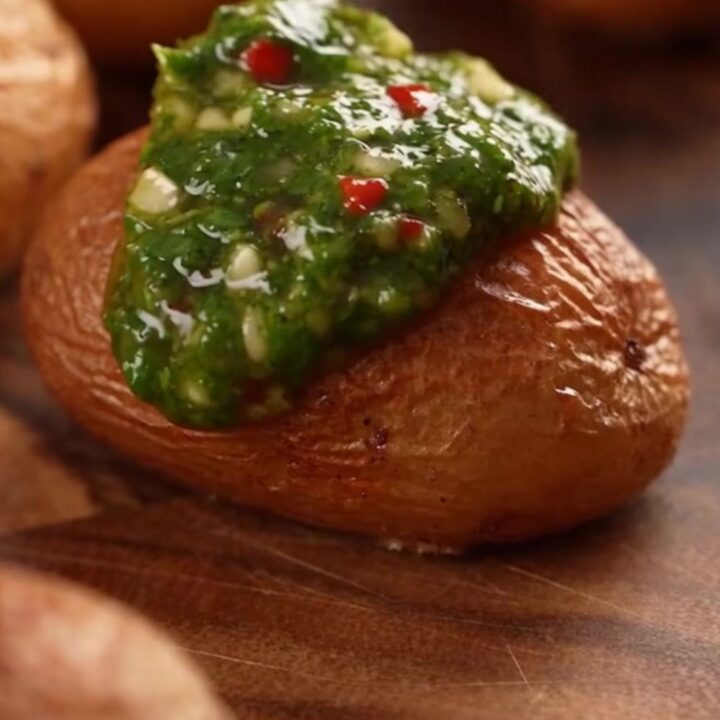 A top-down view of crispy smashed fingerling potatoes on a baking sheet, topped with vibrant green chimichurri sauce.