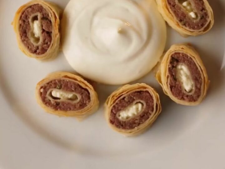 A vibrant plate of Turkish Beyti Sarma kebabs arranged in a circle with garlic yogurt and red tomato butter sauce.