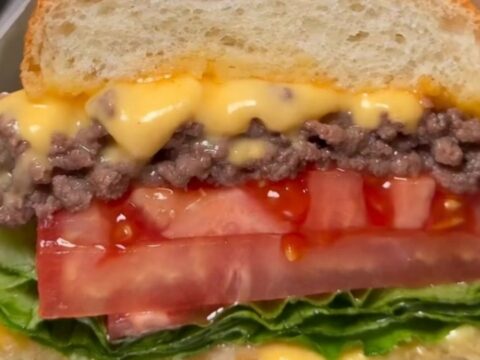A classic NYC chopped cheese sandwich wrapped in butcher paper, showing the melty beef and cheese filling.